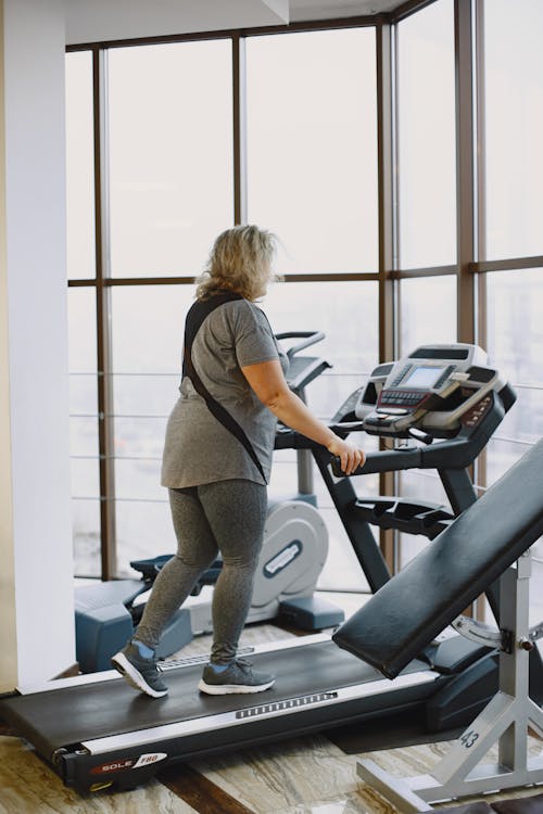 Mujer madura caminando en cinta en el gimnasio - método 12-3-30 mayores 50
